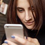 close-up-shot-charming-young-european-woman-holding-generic-cell-phone-checking-email-newsfeed-via-social-media-using-online-apps