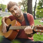 dreamy-relaxed-man-playing-guitar-sit-grass-park-with-instrument