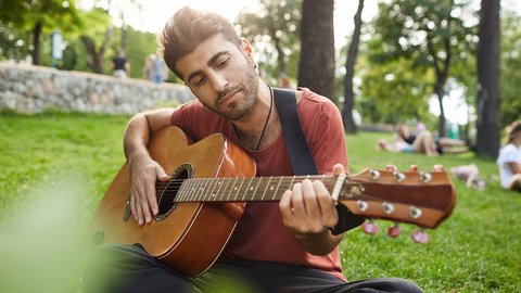 dreamy-relaxed-man-playing-guitar-sit-grass-park-with-instrument