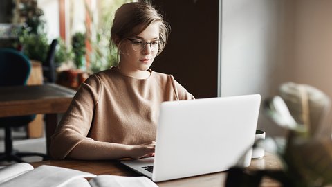 work-lifestyle-business-concept-good-looking-focused-european-female-trendy-glasses-sitting-cafe-near-laptop-working-notebook-surrounded-with-books-making-notes