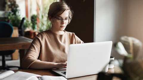 work-lifestyle-business-concept-good-looking-focused-european-female-trendy-glasses-sitting-cafe-near-laptop-working-notebook-surrounded-with-books-making-notes